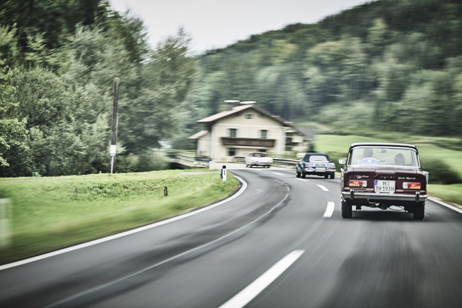 Three classic cars drive on a country road