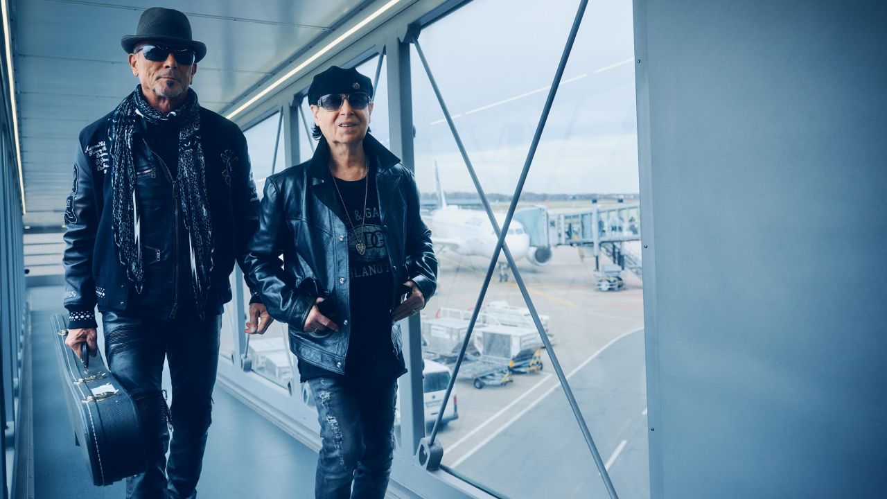 Zwei Mitglieder der Band Scorpions in schwarzen Lederjacken und Sonnenbrillen gehen über Gangway am Flughafen