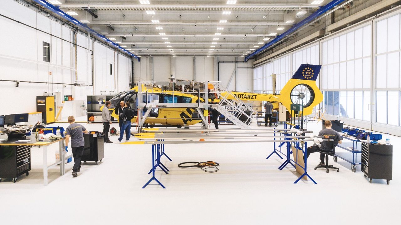 Techniker arbeiten in einer großen Wartungshalle an einem gelben ADAC-Rettungshubschrauber.