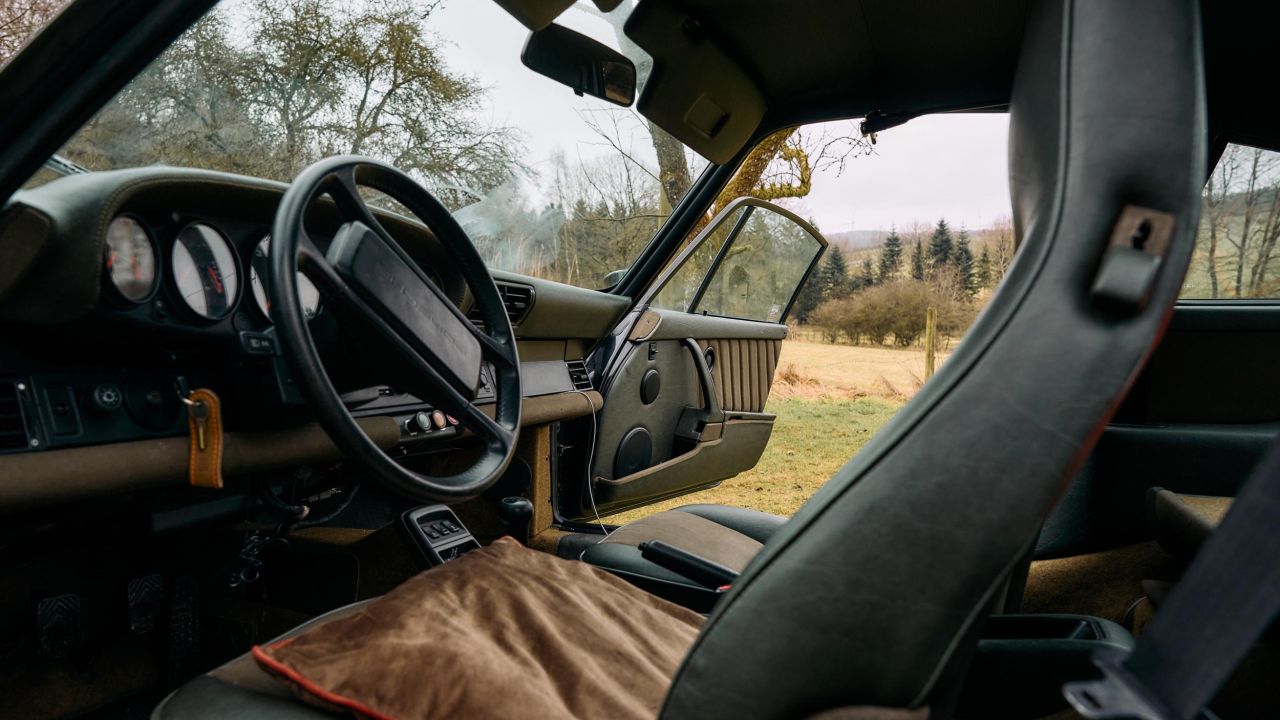 Interior view of a green Porsche 911 with black leather seats, beige seat cushions, and open door
