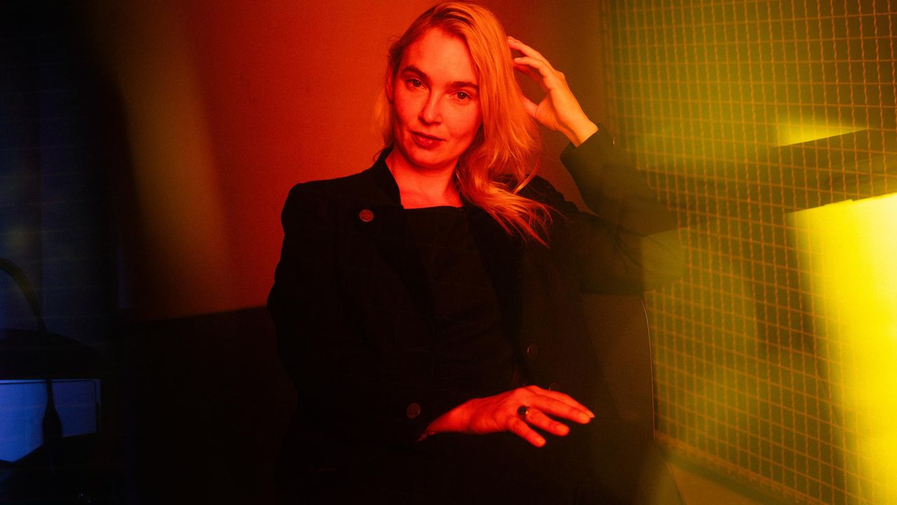 Portrait of a woman in a dark suit, sitting in a room with intense red and yellow lighting